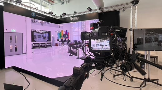 The University of Portsmouth Centre for Creative and Immersive Extended Reality (CCIXR). A high tech camera is positioned in front of a 3D 'smart stage' with computer generated images on two screens and the floor
