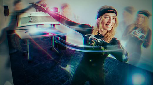 A person with long hair wears a lycra motion capture suit, gloves and headband and swings their arms to convey movement